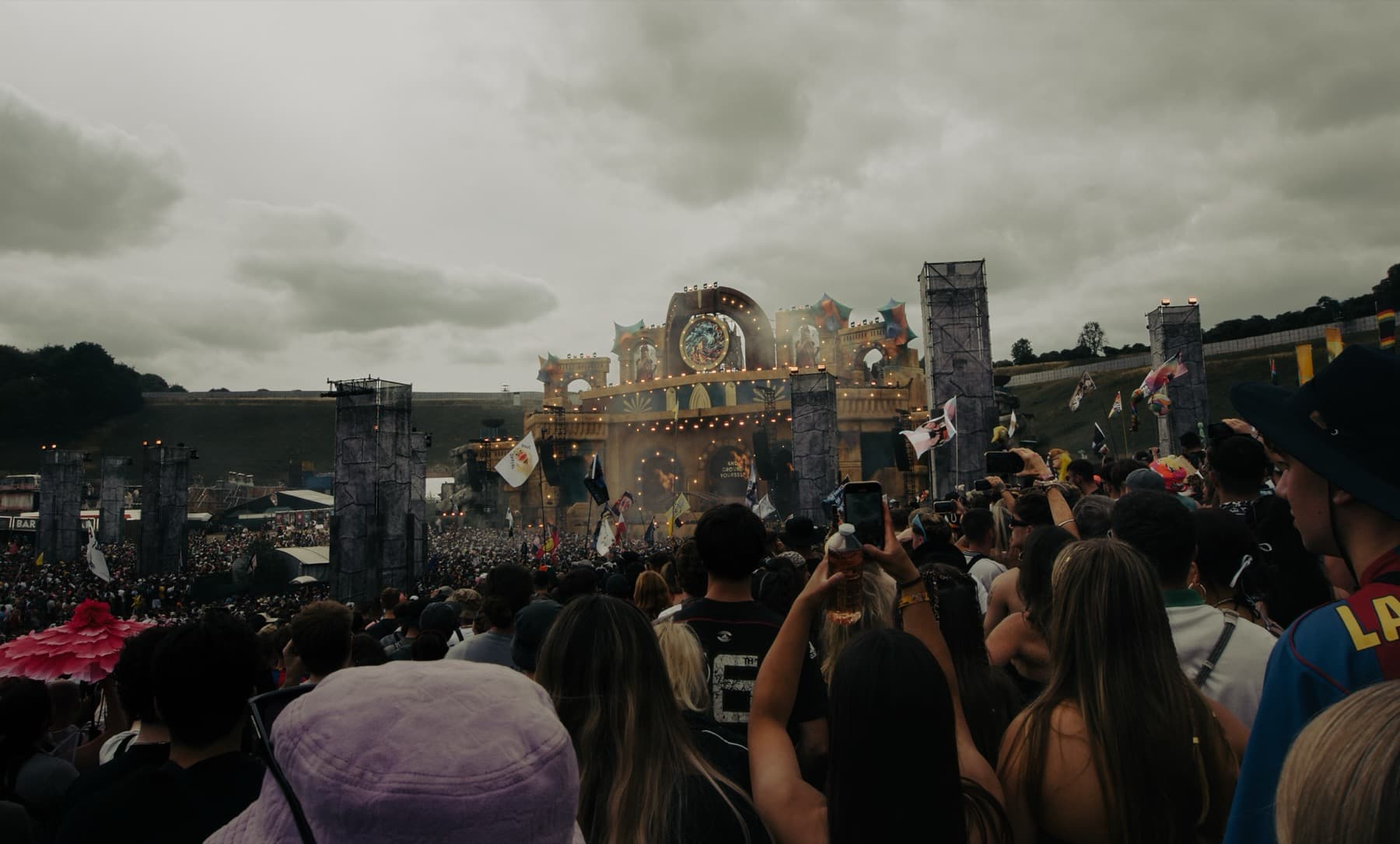 Wide view of thousands gathered before the ornate main stage under dramatic overcast skies with flags waving