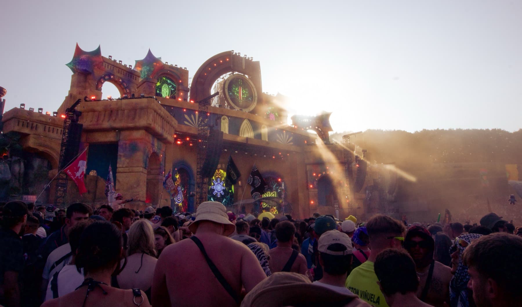 Huge crowd facing an ornate castle-themed main stage at golden hour with dust rising in the sunlight