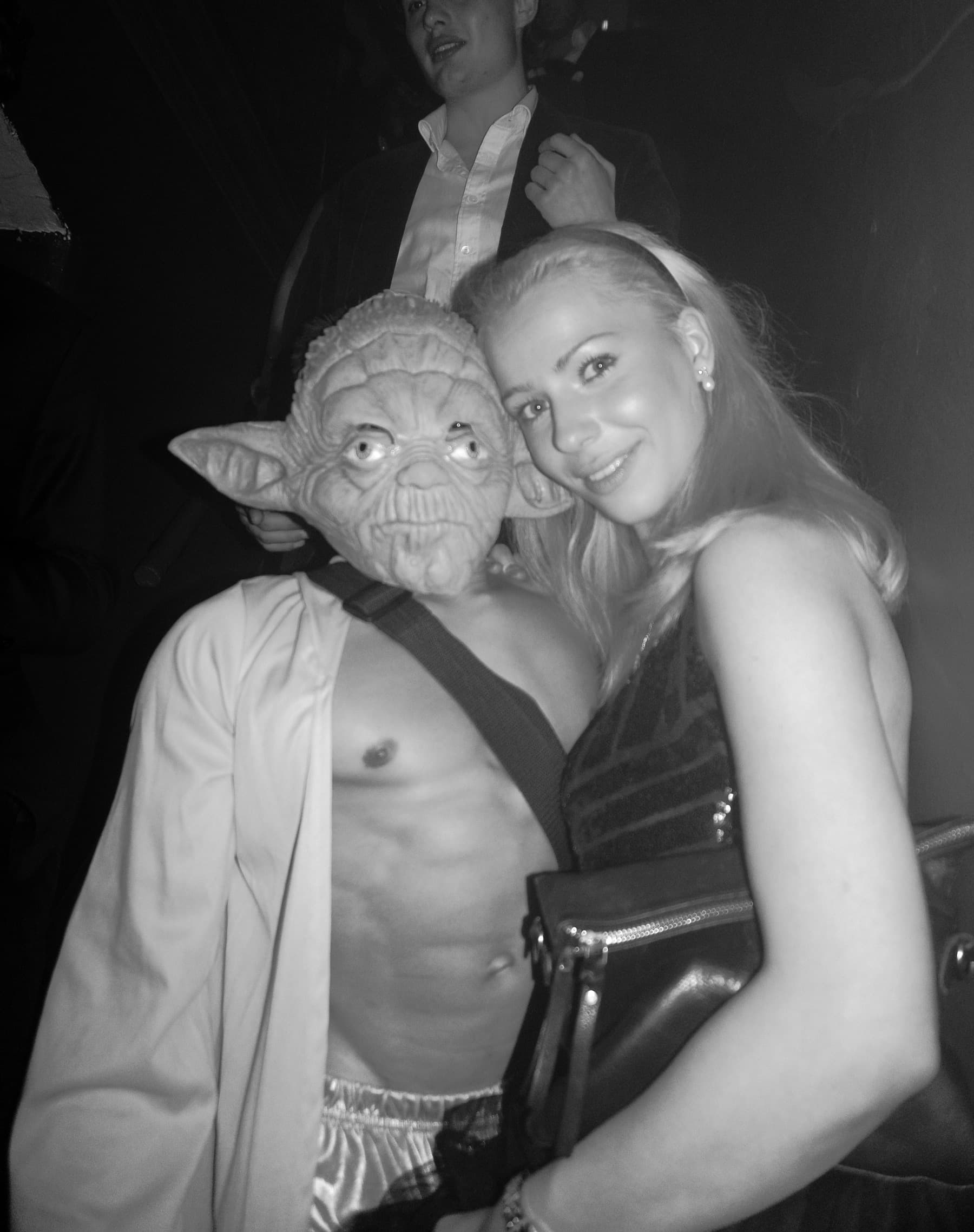 Partygoer in a Yoda mask with an open robe posing beside a smiling woman in black and white