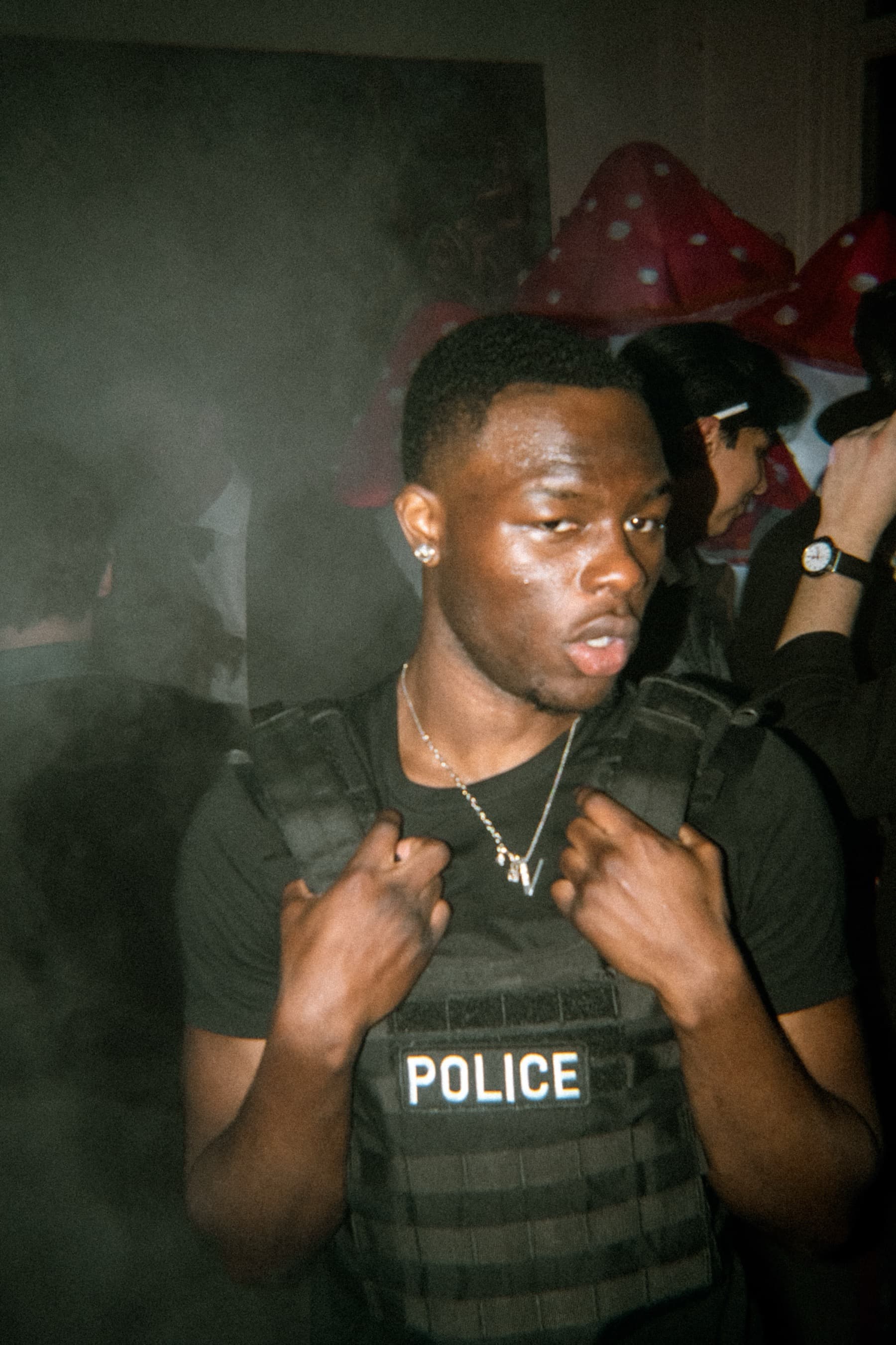 Guest in a police vest costume posing through haze with mushroom decorations behind
