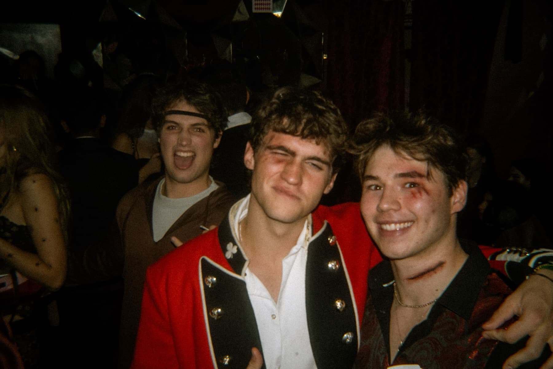 Three friends in costume including a red military jacket and fake wound makeup posing arm-in-arm