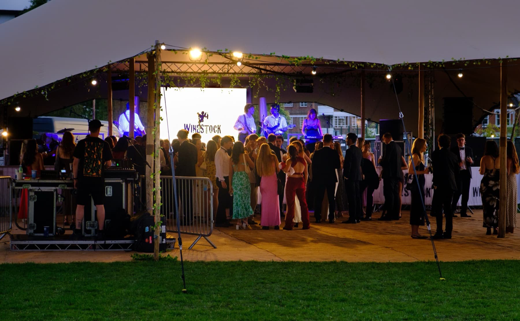 Guests gathered on a dance floor under a stretch tent with the lit Winestock stage backdrop at dusk