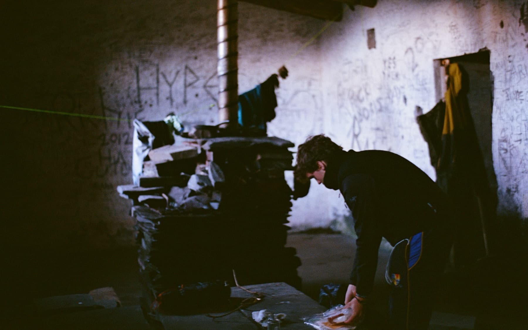 Person unpacking gear inside a graffiti-covered quarry building with a washing line strung across the room, shot on film
