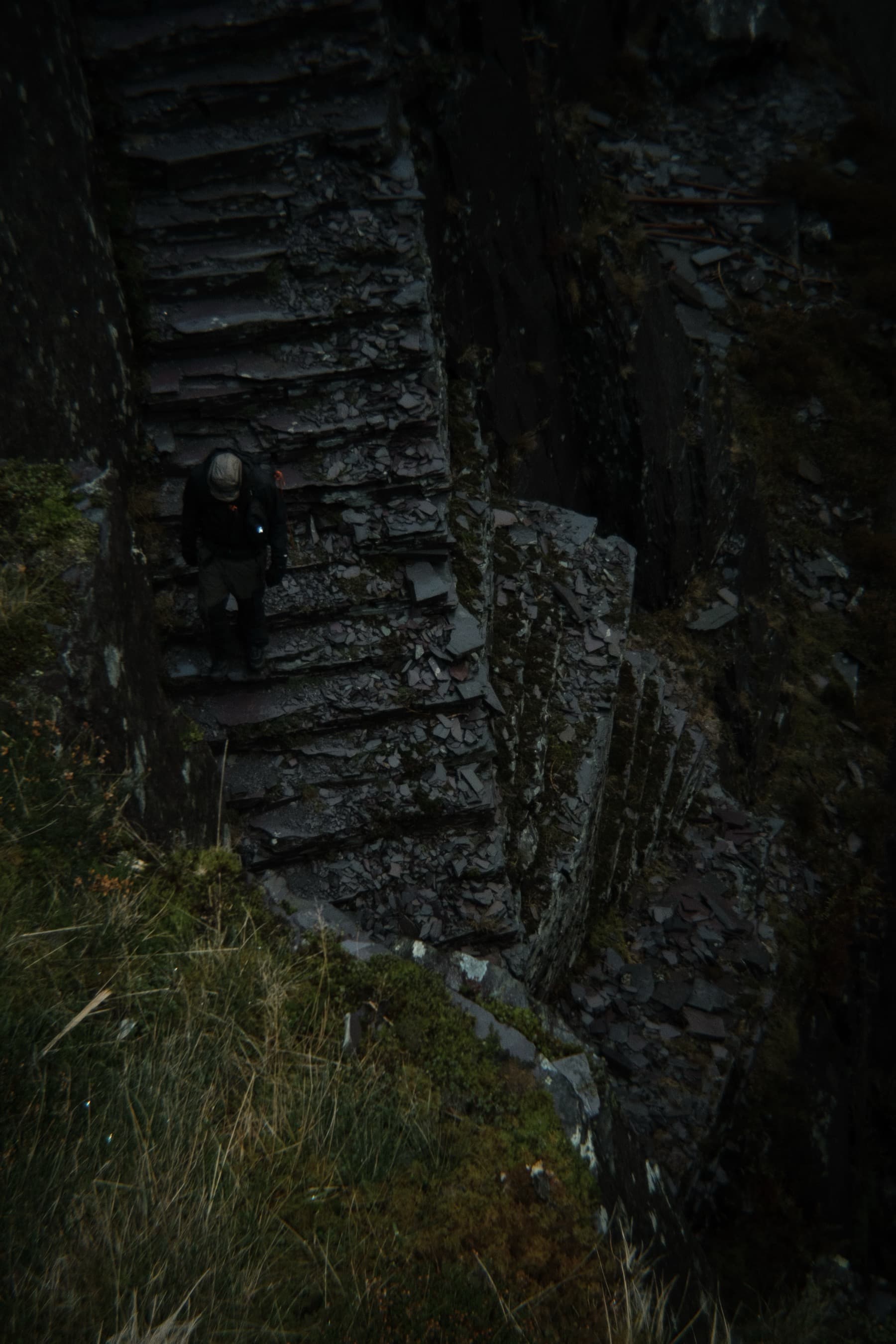 Person climbing steep slate steps on a dark quarry incline surrounded by rough-cut rock walls