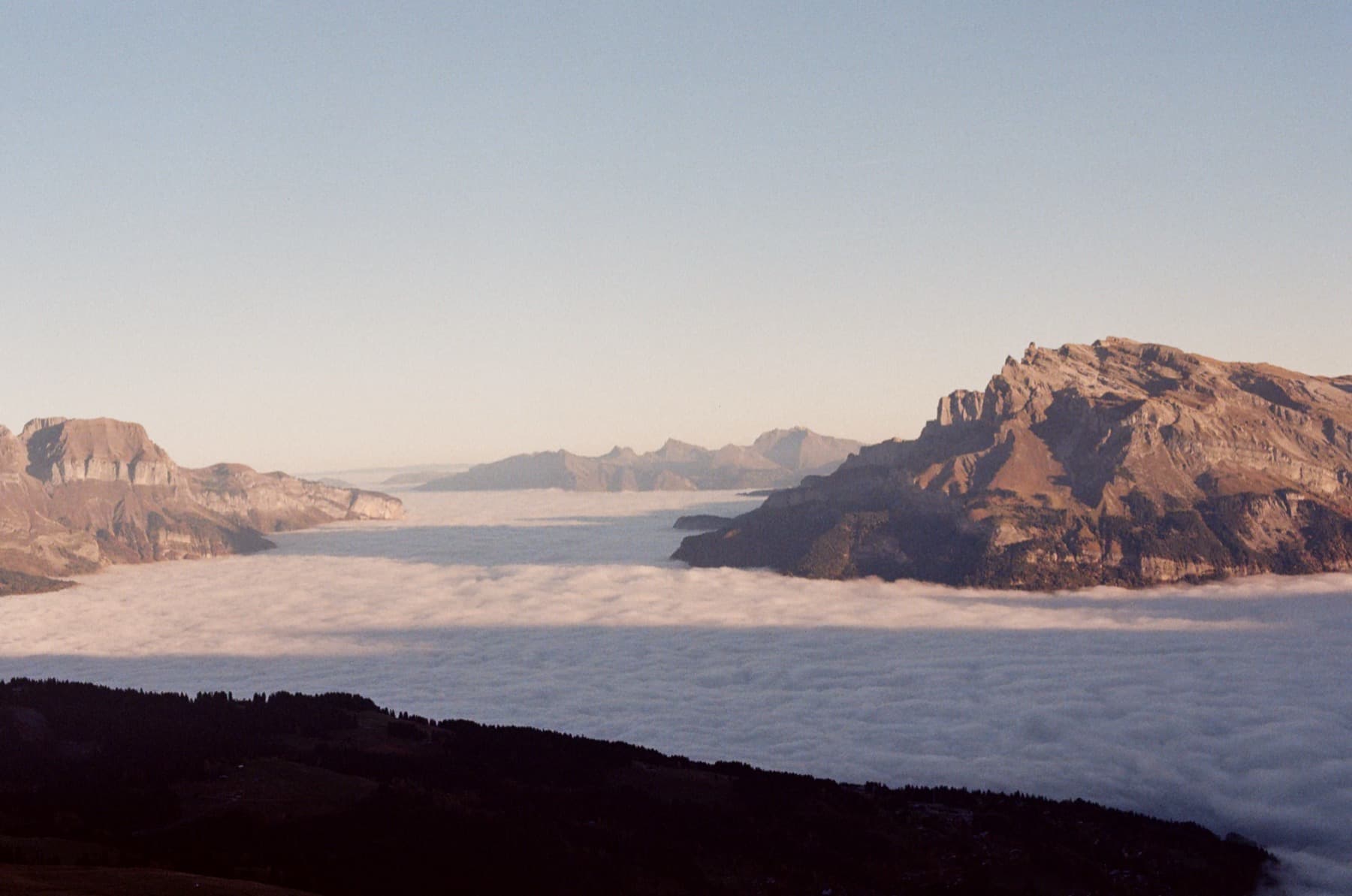 A sea of clouds filling the valley below with rocky mountain summits emerging like islands in warm morning light, shot on film