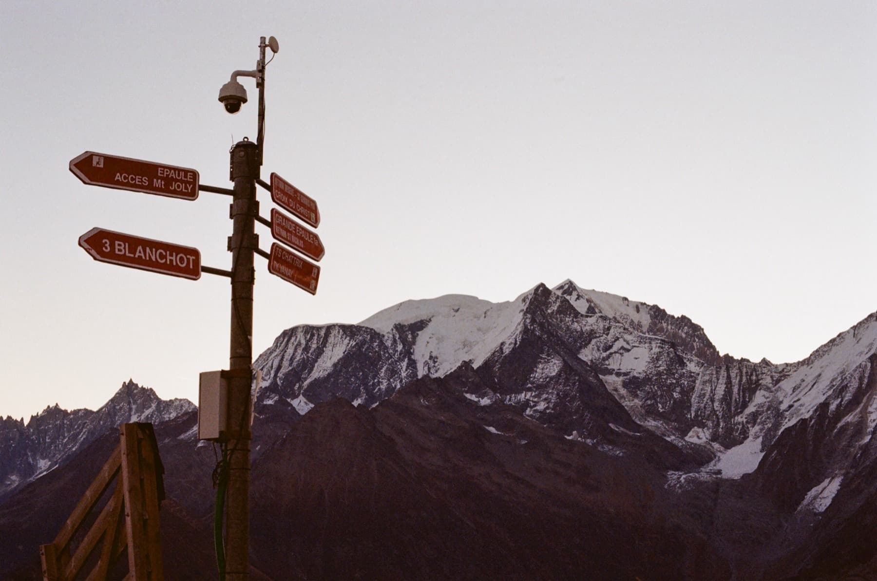 Trail signpost for Mont Joly and Blanchot with the snow-covered Mont Blanc massif looming behind in soft twilight, shot on film