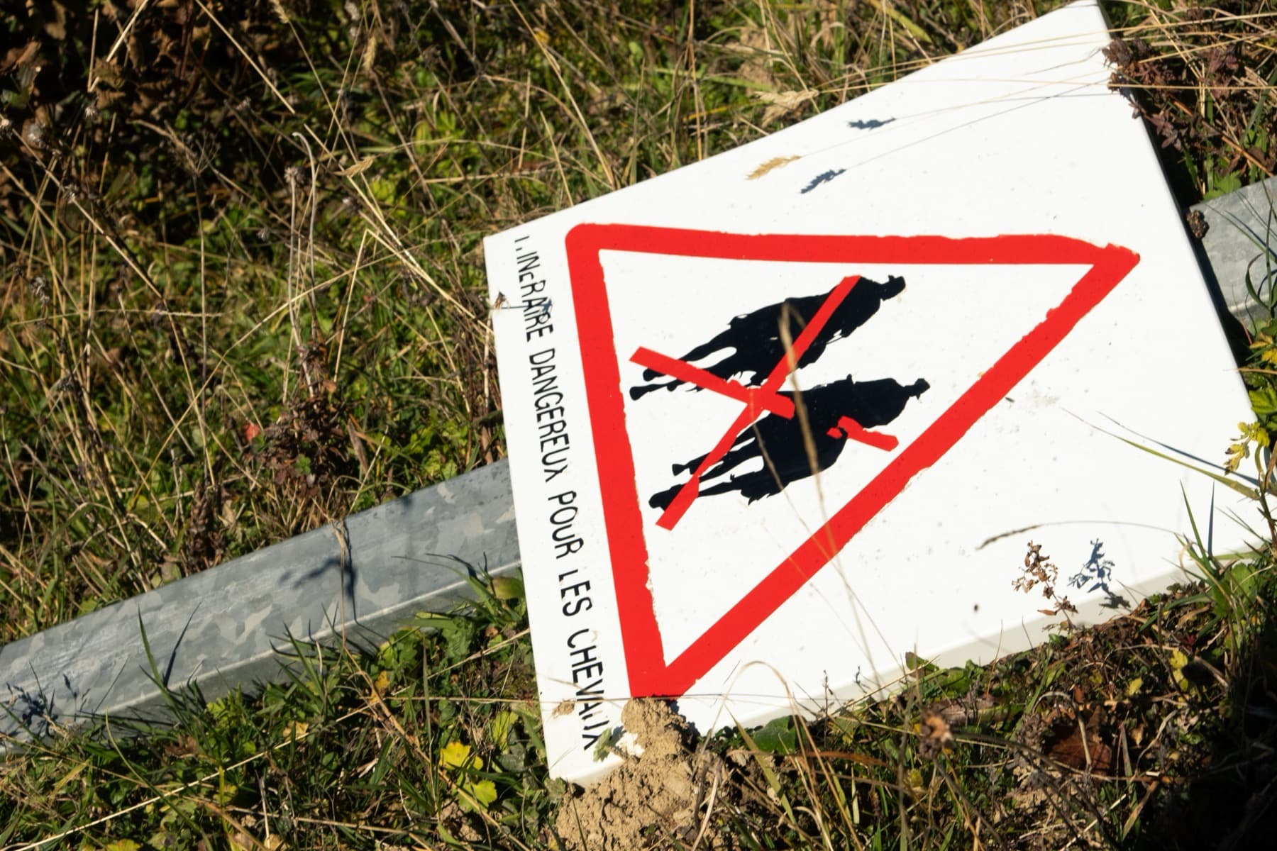 A fallen French warning sign for hikers lying in the grass on a sunny Alpine hillside