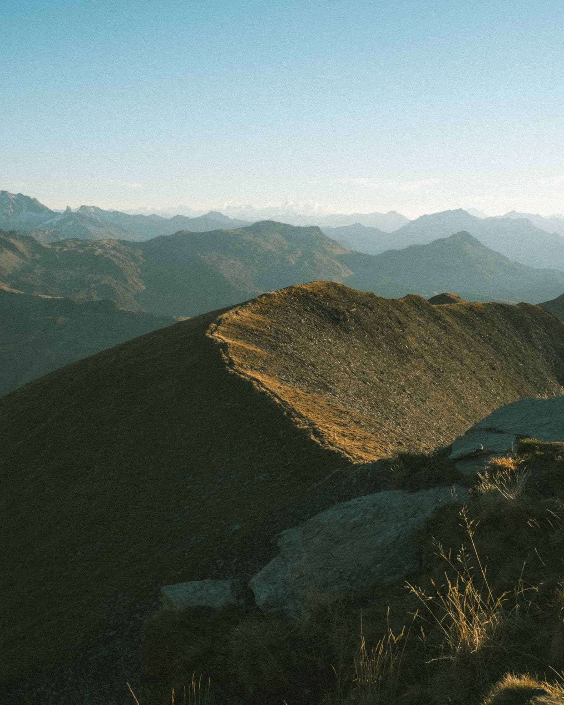 Sunlit ridge leading to the summit of Mont Joly with an endless layered panorama of Alpine peaks fading into the morning haze