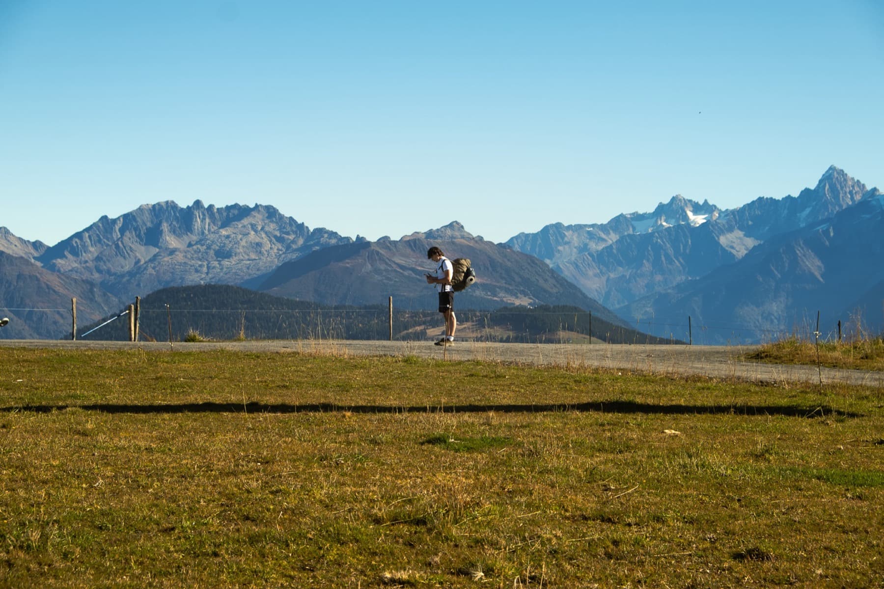 A lone hiker with a backpack checking a map on an open alpine meadow with a panoramic view of rugged mountain peaks beyond