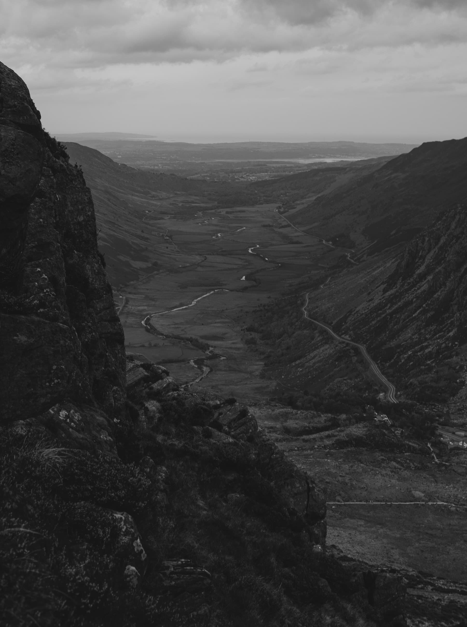 Sweeping valley view from a rocky vantage point with a winding river and road far below in black and white