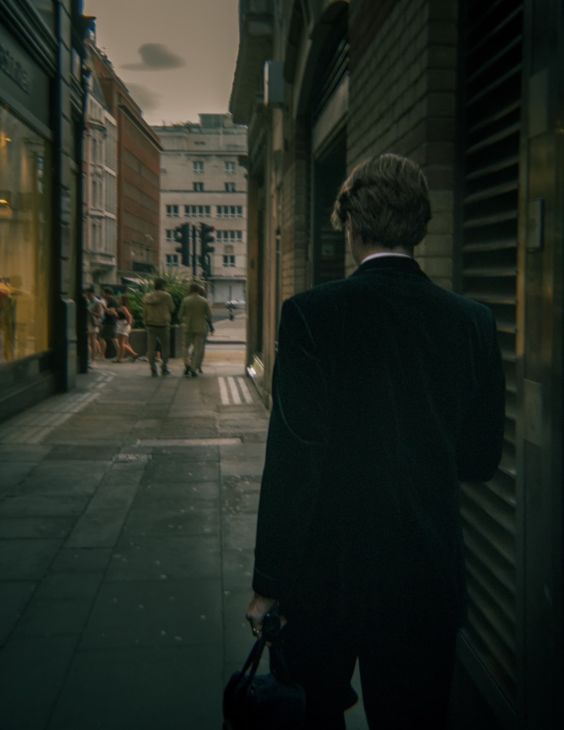 Man in a dark suit carrying a bag walking away down a London street with pedestrians in the background