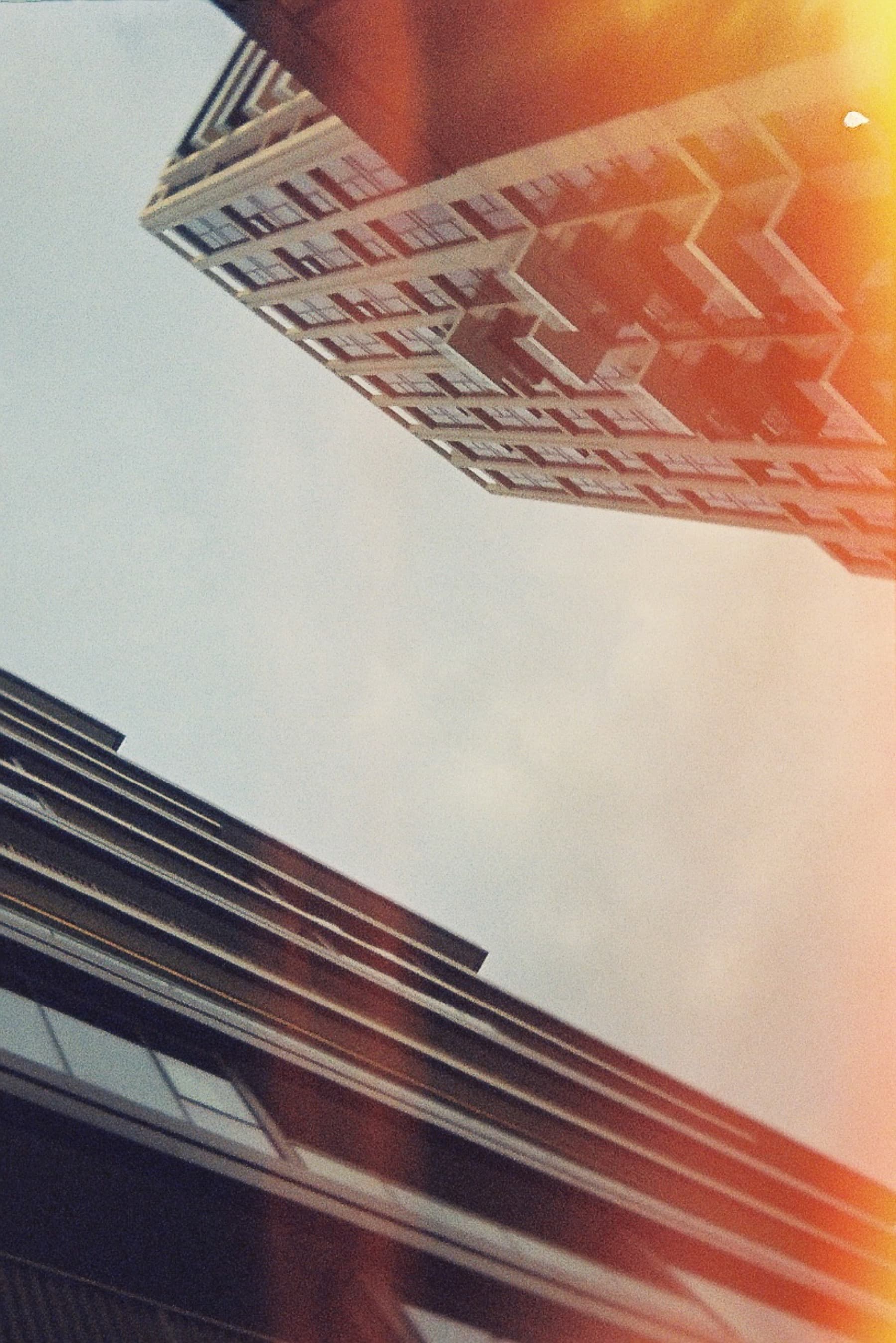 Looking up at apartment buildings from street level with golden sun flare and warm light leak on film