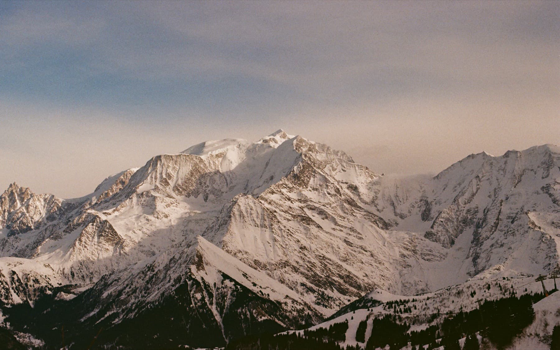 Dramatic panoramic view of the Mont Blanc massif with snow-covered ridges and exposed rock faces under a hazy winter sky